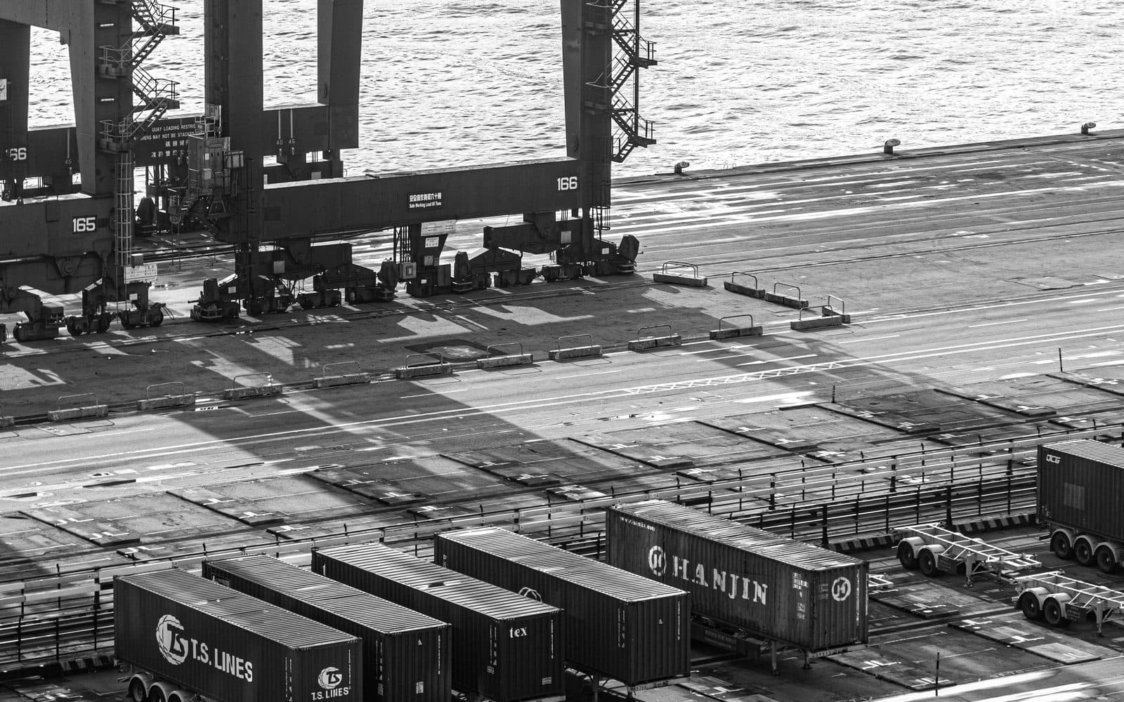Gantry cranes loading shipping containers at a port terminal as a container truck departs
